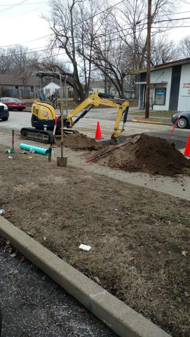 Commercial plumber in Evansville, IN — excavator and green sewer pipe at a street cut