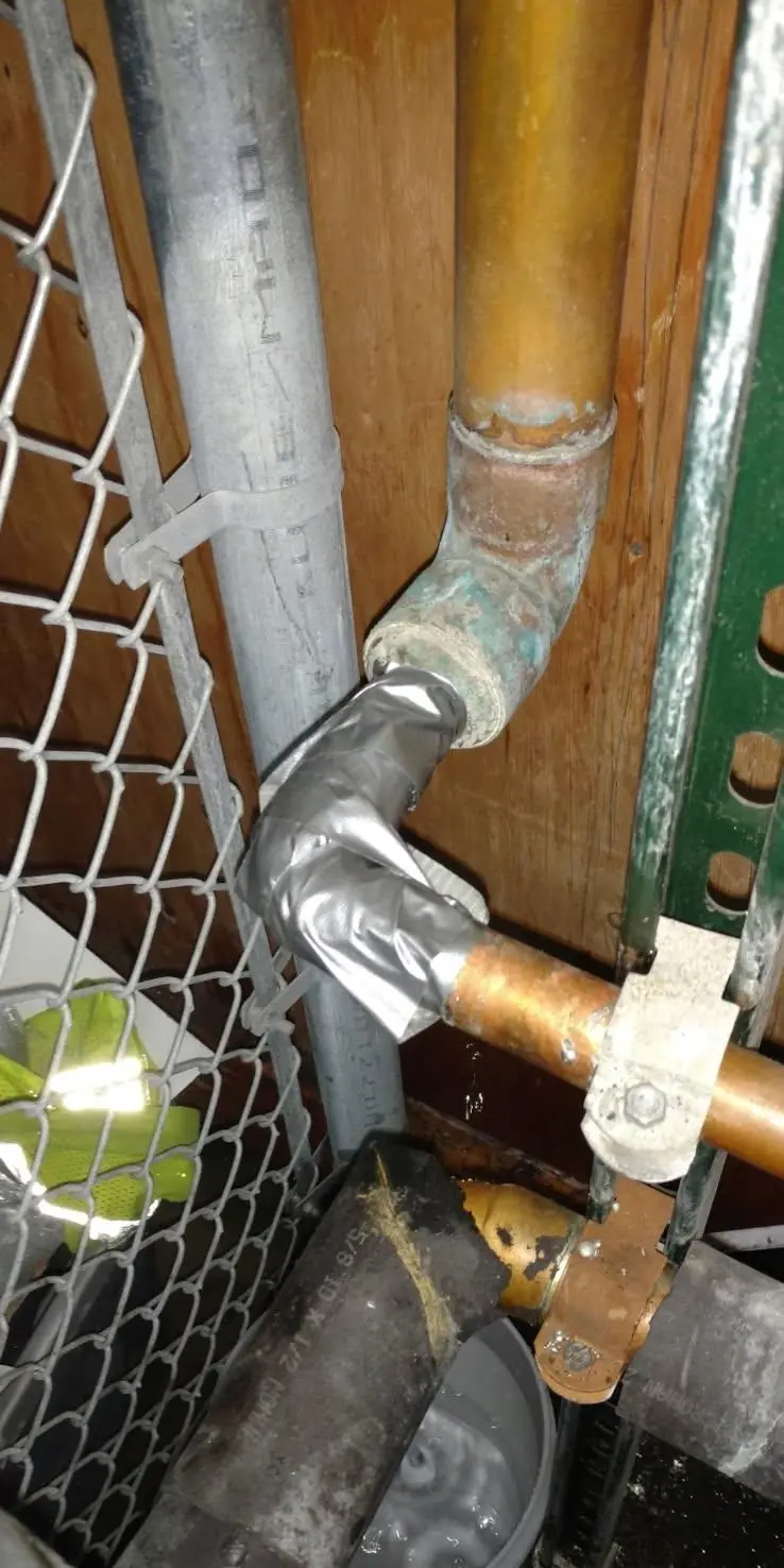 Plumbing pipe repair in Evansville, IN — corroded copper elbow with tape on the fitting and a bucket catching water