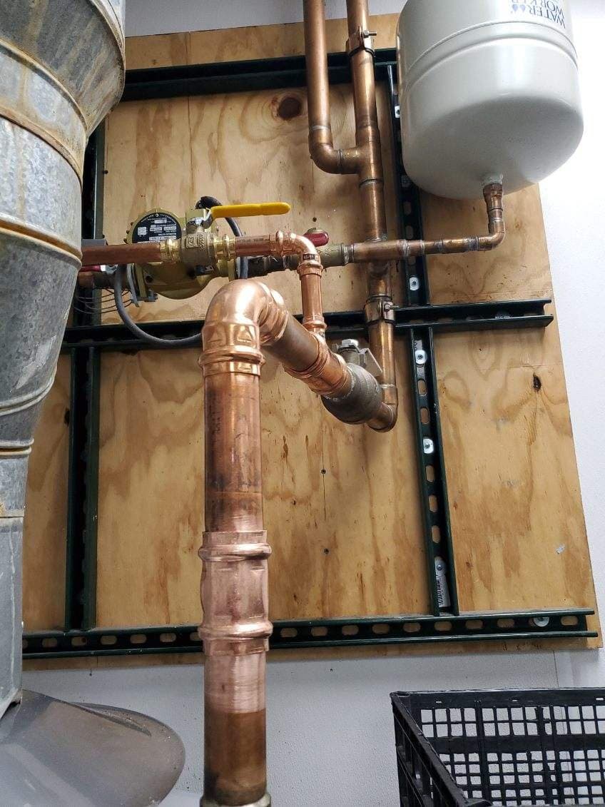 Expansion tank install in Evansville, IN — white expansion tank on copper water lines against a plywood wall
