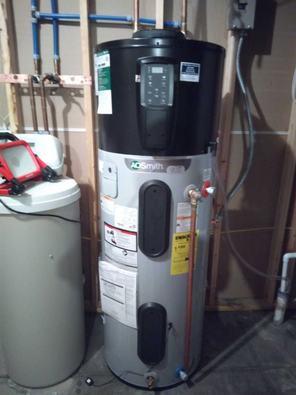 Heat pump water heater and water softener installed side by side against open wall studs