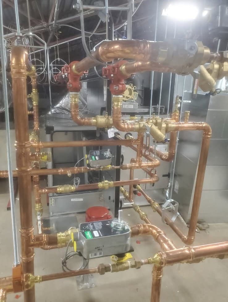 Commercial plumber in Evansville, IN — copper piping rack with brass valves and a pump
