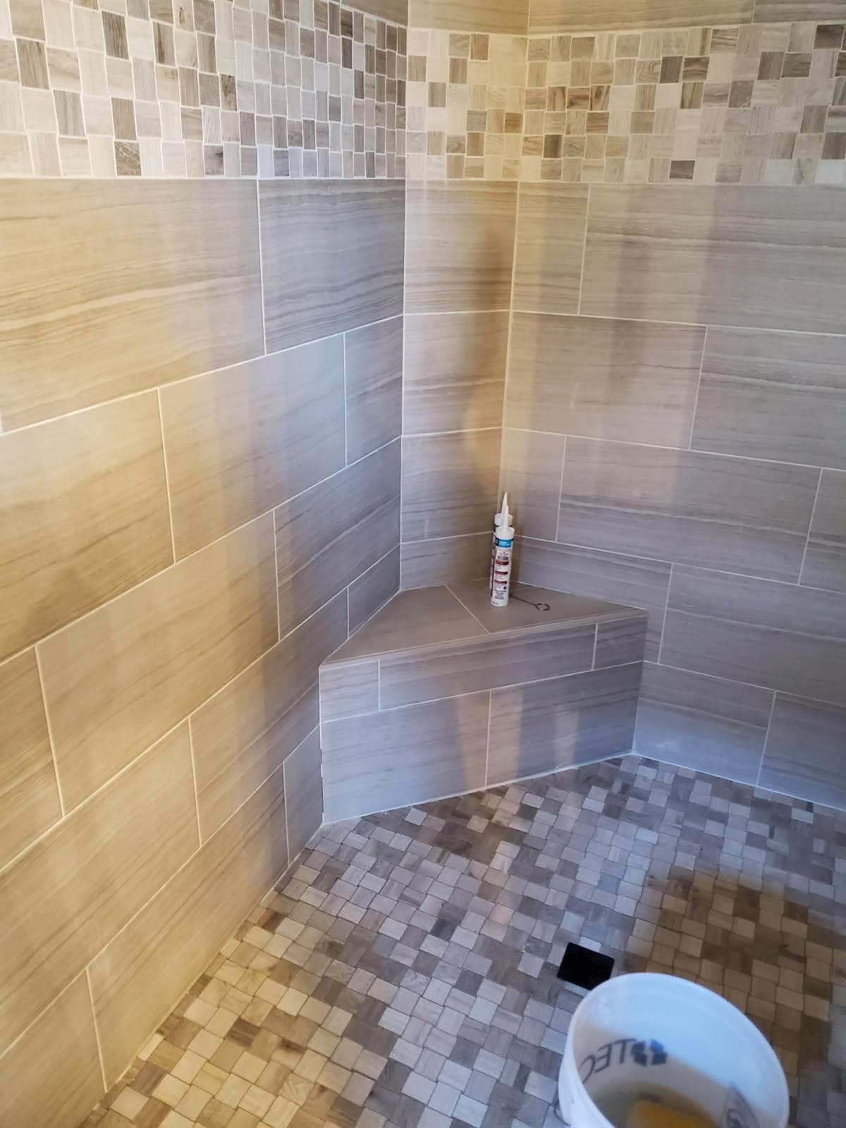 Residential plumber in Evansville, IN — tiled shower with mosaic accent, corner bench, and floor drain